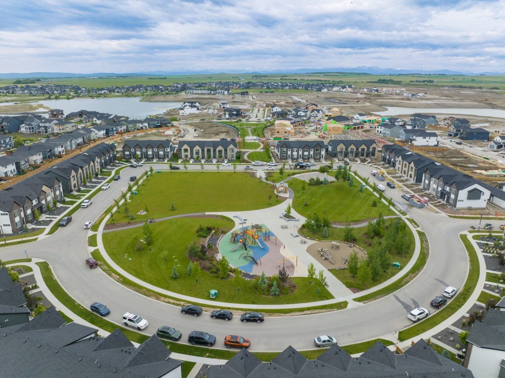 Aerial view of a the Harmony neighborhood with townhouses surrounding a large central park that has a playground, walking paths, and landscaped areas.
